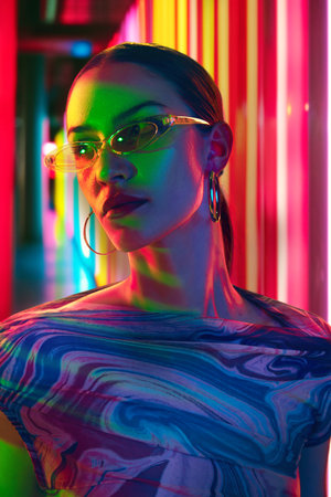 Fashion-forward woman adorned in modern sunglasses posing in mixed vibrant light against vivid backdrop of neon stripes. Concept of youth, beauty, fashion and style, modern lifestyle. Adの写真素材