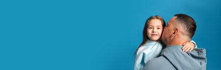 Banner. Father kissing his beloved little child, charming girl to cheek against blue studio...