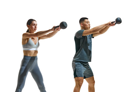 Two fitness enthusiasts wearing fashion clothes in middle of kettlebell workout against white studio background. Concept of people in sport, healthy lifestyle, teamwork, motivation. Adの写真素材