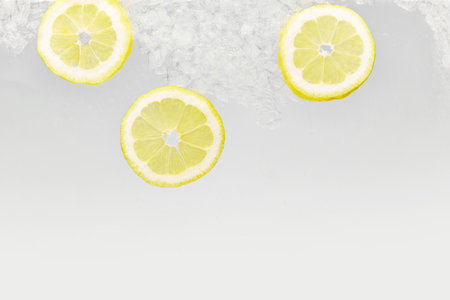 Close up shot of slices of lemon with ice floating in glass of water. Refreshing and detoxed drinks. Textured photo. Abstract wallpaper. Concept of food and drinks, summer,vitamins, nutrition.の写真素材