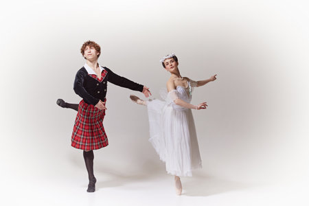 Poised Devotion. ballerina in an ethereal white gown and floral headpiece synchronizing moves with her partner against white studio background. Concept of art, grace and elegance.の写真素材