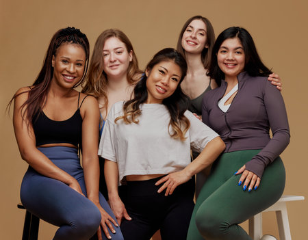 Group of women, representing range of body types and ethnicities posing exude happiness and support against beige studio background. Concept of beauty, unity, wellness, body positivity, diversity.の写真素材