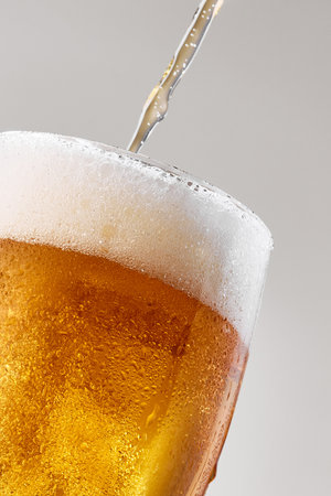 Macro shot captures lager cold golden beer pouring into glass against grey studio background. Concept of food and drink, celebration, Oktoberfest, beverage industry. Adの写真素材