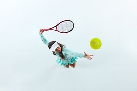 Aerial view of female tennis player, sportsman in mid-action, serving ball against white studio background. Concept of professional sport, championship, active lifestyle, tournament. Adの写真素材