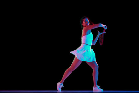 Female athlete in white dress swings her racquet to make powerful shot in neon light against black...