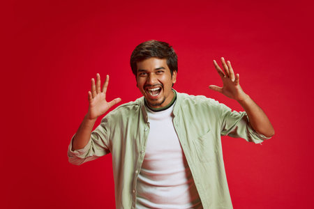 Shouting of joy young Indian man raising hand of excitement against red studio background. Black Friday mood. Concept of fashion and style, human emotions, sales season, Cyber Monday.の写真素材