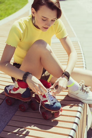 Young girl, teenager preparing to skate on vintage roller skaters, sitting on bench and change shoes...