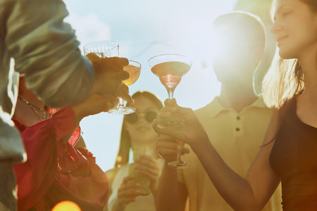 Photo of joyful toast among friends, their faces beaming with happiness and drinks shimmering in sunlight. Concept of party, Friday mood, celebration, summer holidays, relax.の写真素材