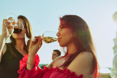 Group of friends enjoys sunny day together, raising their glasses in joyful toast and drinks sweet and sour cocktails. Concept of party, Friday mood, celebration, summer holidays, relax.の写真素材