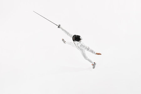 Aerial view of young man, fencer in uniform leaping to attack opponent against white studio background. Activity. Concept of professional sport, healthy lifestyle, competition, achievement. Adの写真素材