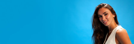 Banner. Young brunette woman looking at camera against blue studio background with negative space to insert text. Trendy colors. Concept of human emotions, fashion and style, business.の写真素材