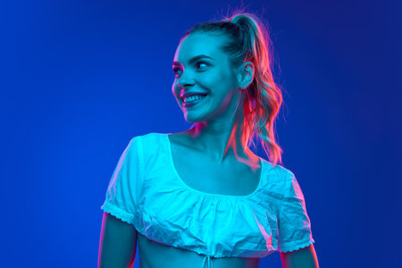 Portrait of young attractive woman looking away with wide smile in neon light against gradient...