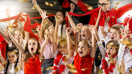 Group of excited children cheering, waving red scarves and wearing red and white outfits. Confetti fills air, capturing joy and energy of celebration. Concept of sport, match, competition, support. Adの写真素材