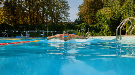 Wearing goggles, swimmer powers through water with butterfly stroke, demonstrating strength and...