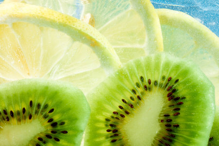 Slices of kiwi and lemon float in sparkling bubbles, creating refreshing and vibrant scene against bright blue background. Textured wallpaper. Concept of summer, nutrition, diet, healthy, detoxの写真素材