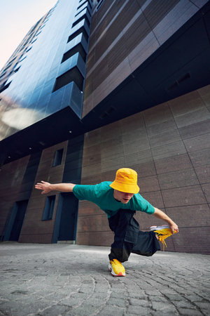 Young man, fashionista in colorful attire, breakdancer posing against urban background with tall, modern architecture. Concept of lifestyle, extreme sport, freestyle, activity, motion. Adの写真素材