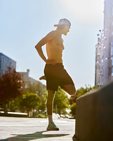 Full-length of shirtless young man in short and cap, training shirtless outdoor on empty street in...