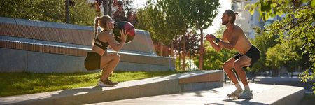 Athletic, fit man and woman training together outdoors in public park in early summer morning, doing...