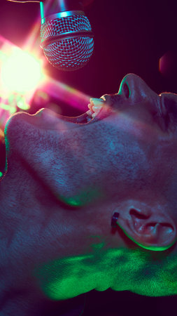 Close-up photo of singers face, his expression full of intensity and passion, bathed in neon lights during powerful performance. Concept of music and party, hobby and work, energy, music festivals.の写真素材