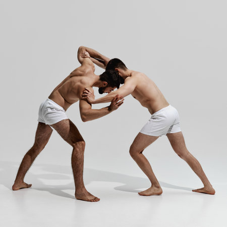 Dynamic wrestling duel unfolds, with two competitors locked in struggle for dominance and victory against warm grey background. Concept of male health, beauty and fashion, fitness, masculinity. Ad.の写真素材
