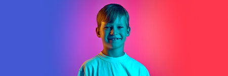 Banner. Happy smiling little boy, preteen looks at camera in neon light against gradient blue-pink studio background. Concept of children, human emotions, fashion and style, lifestyle. Adの写真素材