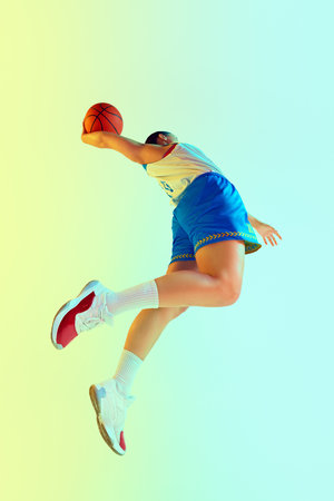 Low angle of basketball player leaping in motion to make perfect goal in neon light against gradient studio background. Concept of professional sport, championship, hobby and recreation. Adの写真素材