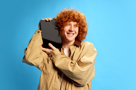 Cheerful smiling red haired, curly man holding tablet with blank screen against blue studio background. Online shopping. Concept of Black Friday, Cyber Monday, fashion, Flash Sale. Adの写真素材