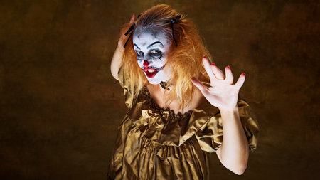 Frightening clown woman in golden gown, raising her hands with wild expression, posing dramatically...