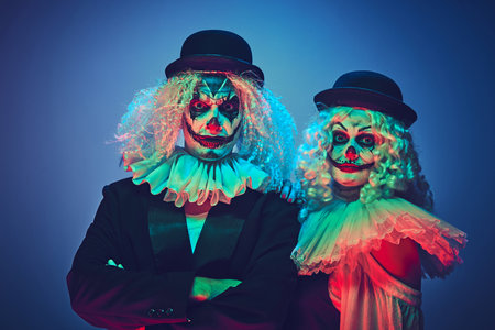Portrait of creepy clown couple dressed retro style clothes posing looking at camera calmly in neon...