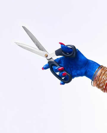 Witchs, monsters blue hand with long, vivid nail art holds scissors against white studio background....