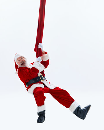 Santa Claus gripping red fabric, with surprised expression, against white studio background, as if hes climbing up chimney. Concept of winter holidays, Holly Jolly mood, celebration. Adの写真素材