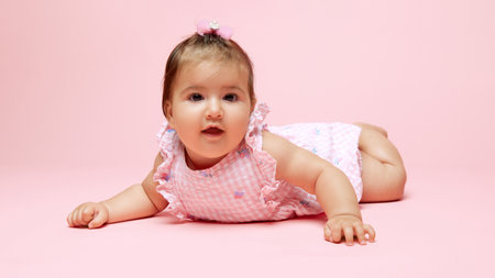 Little cute little princess exploring world, dressed in pink romper with matching bow against soft...