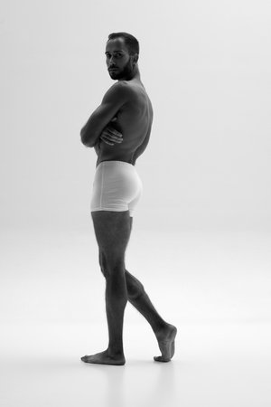 Monochrome portrait of young man posing in briefs, underwear showing his muscular body against white background. Concept of beauty and fashion, style and youth, male health.の写真素材