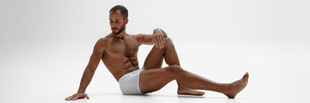 Banner. Young man sitting on floor, posing in underwear shows his muscular body against white background with negative space. Concept of beauty and fashion, style and youth, male health.の写真素材