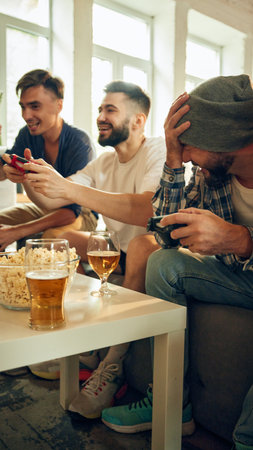 In full swing, everyones smiles contagious as they compete. Cozy setting with beers and snacks keeps mood friendly and upbeat. Concept of football fans, sport evens, video games and cybersport.の写真素材