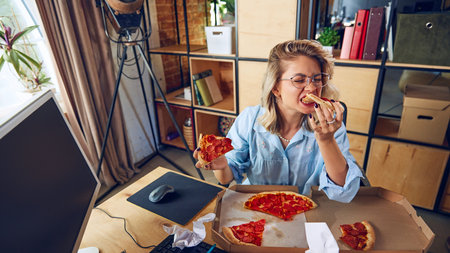 Young woman enjoying pizza while working, during important meeting. Her focus on food rather than work highlights bad multitasking habits. Concept of business, people and daily work challenges. Ad.の写真素材