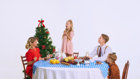 Girl is full of excitement, standing by tree, sharing her joy with her family during holiday meal. Table filled with treats and decorations. Concept of celebration, holiday, family meal, Christmas.の写真素材