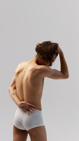 Back view of young man in underwear with hands behind back against grey studio background. Emphasizes natural physique. Concept of natural beauty, male health, fashion, skin care. Adの写真素材