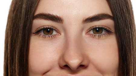 Close-up photo of young woman with bright brown eyes, long lashes and smooth facial skin against...