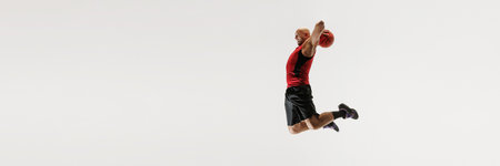 Male athlete dressed in tank top and athletic shorts leaps high, aiming to dunk basketball against...
