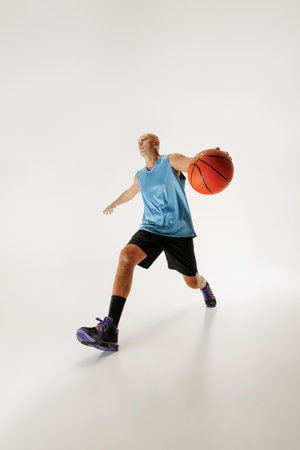 Middle aged basketball athlete dressed in sportswear dribbles basketball, ready to make shot against grey studio background. Concept of sport event, competition, active and healthy lifestyle, game.の写真素材