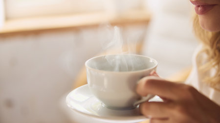 Close-up shot of woman with steaming cup of coffee, capturing warmth and relaxation in softly lit room. Concept of wake up, beauty, weekend, morning routine, home.の写真素材