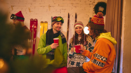 Cheerful holiday gathering with friends in bright ski clothes laughing and toasting, surrounded by warm glow from candles, string lights, and festive decor. Concept of holidays, Christmas party. Adの写真素材