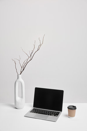 Laptop, coffee cup, and white vase on clean desk. Balanced composition with room for overlays. Ideal for marketing or business mockups. Concept of business, marketing, aesthetic, promoting.の写真素材