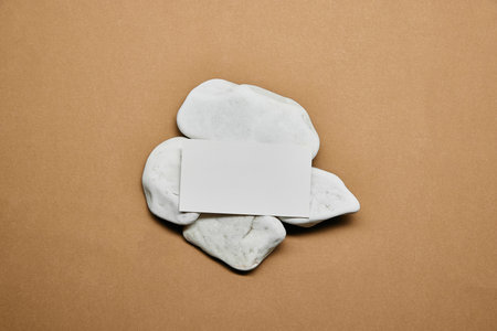 Flat arrangement of blank card on white stones, centered on warm beige surface against minimalist style. Negative space to insert text. Concept of business, marketing, aesthetic, promoting.の写真素材