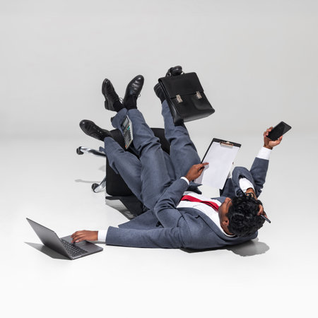 Work pressure and chaotic office environments. Professional man in suit sprawls on chair, managing phone, clipboard, and briefcase. Concept of business, professionalism, multitasking. Adの写真素材