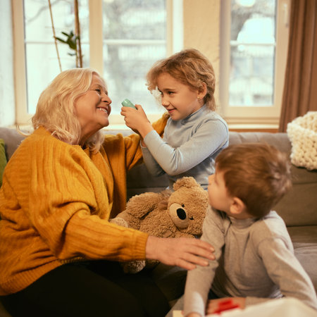 Boy playfully examines grandmothers heartbeat while girl holds teddy bear, combining learning with imaginative play to understand medicine. Concept of knowledge about healthy lifestyle.の写真素材