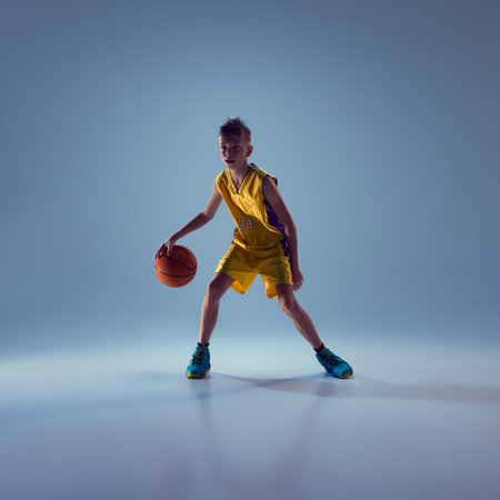 Little boy dressed in sport uniform training basketball techniques against grey studio background. Concept of sport, leisure activity, hobby, competition.の写真素材