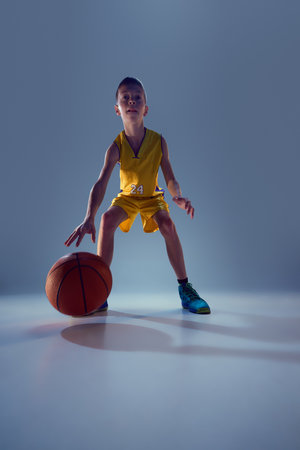 Low angle view of teen boy, competitive basketball player dribbling in motion against grey studio background. Basketball techniques. Concept of sport, leisure activity, hobby, competition.の写真素材