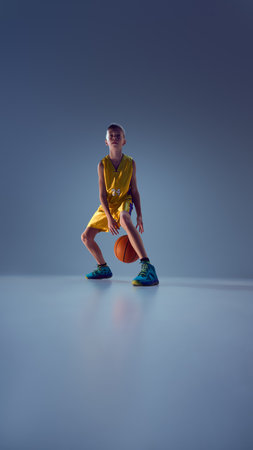 Sportive teenage boy, playing basketball using different techniques to confuse opponent and win match against grey studio background. Concept of sport, leisure activity, hobby, competition. Adの写真素材